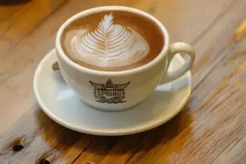 Secangkir kopi dengan latte art di atas meja kayu
